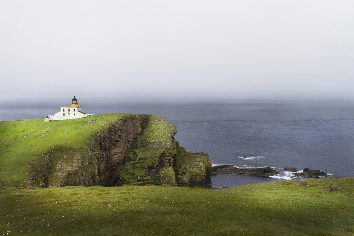 White lighthouse atop a grassy cliff edge above the sea