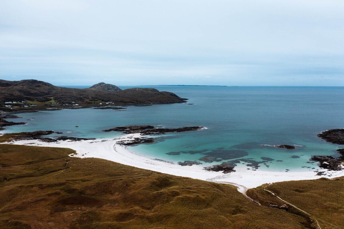 Curved white sand bay meets turquoise water below coastal hills