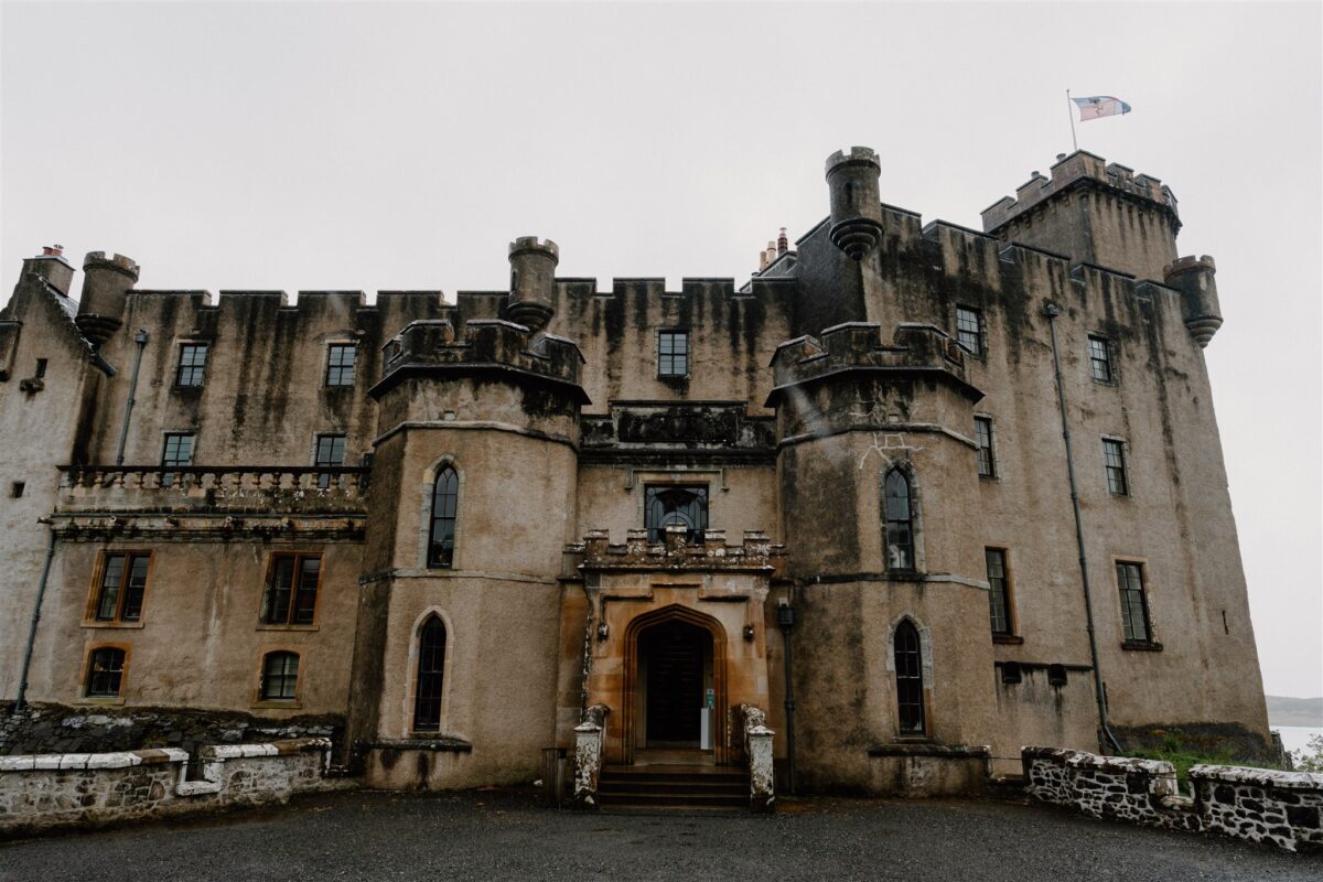 Turreted stone castle with arched entrance and flag flying on a grey day