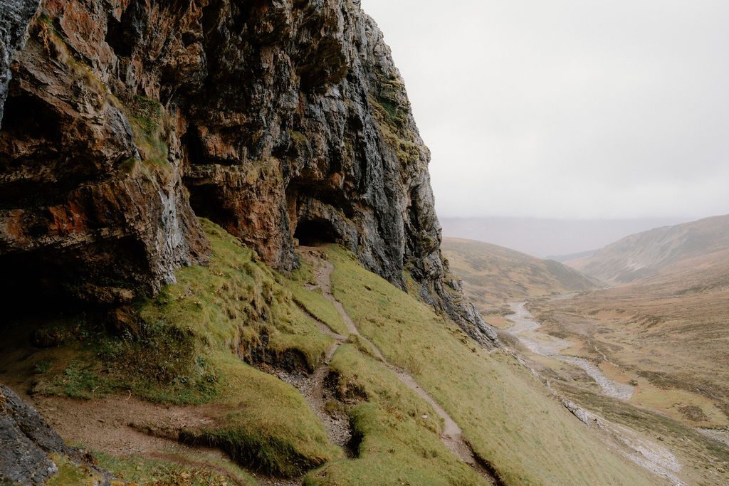 Rocky overhang above a grassy slope overlooking a misty glen