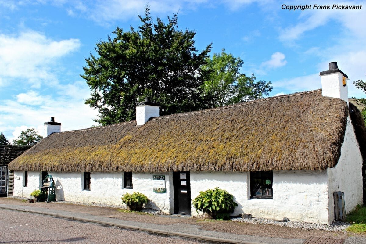 Thatched white cottage with black door, chimneys and roadside pavement