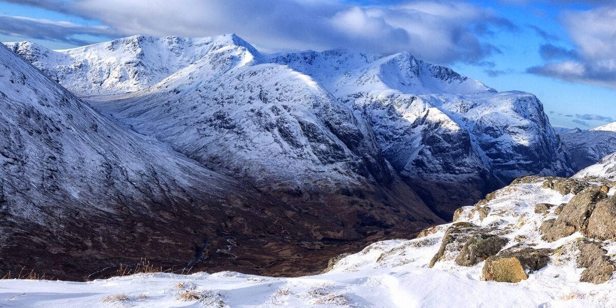 Snow on the mountains of Glen Coe under a blue sky.