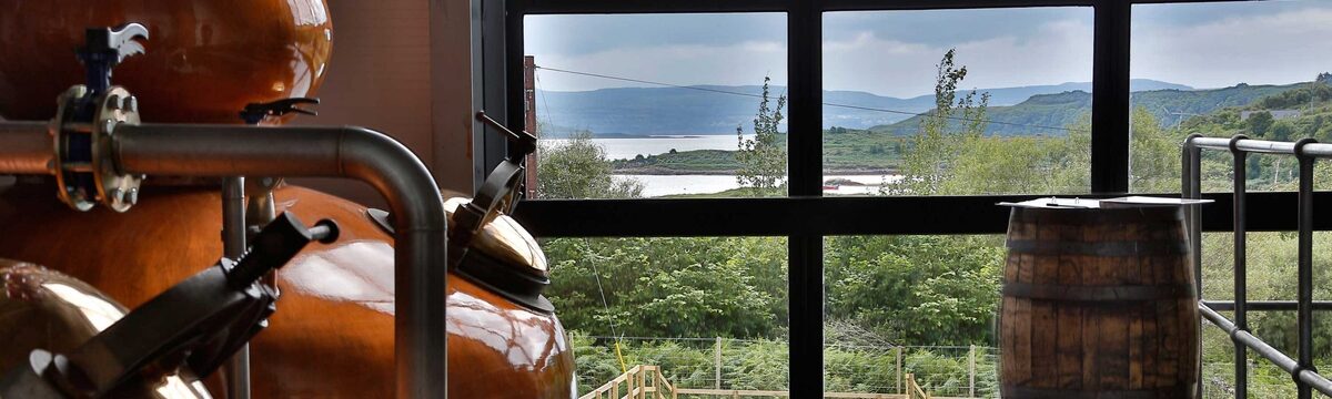 Copper pot still and oak barrel beside a window overlooking a loch