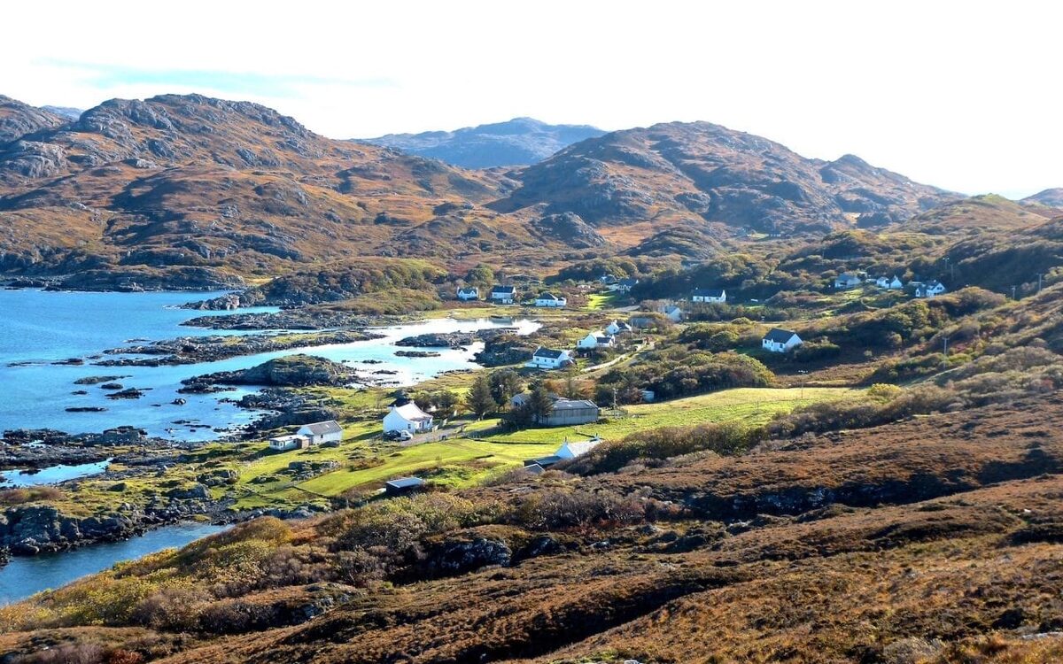 White cottages scattered along a sea loch shore beneath rugged hills