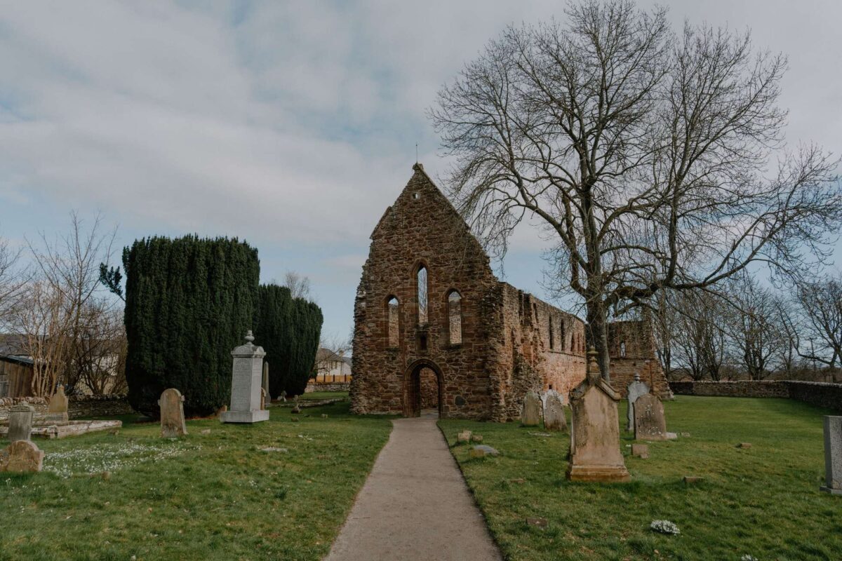 Ruined stone chapel with arched windows surrounded by gravestones and bare trees