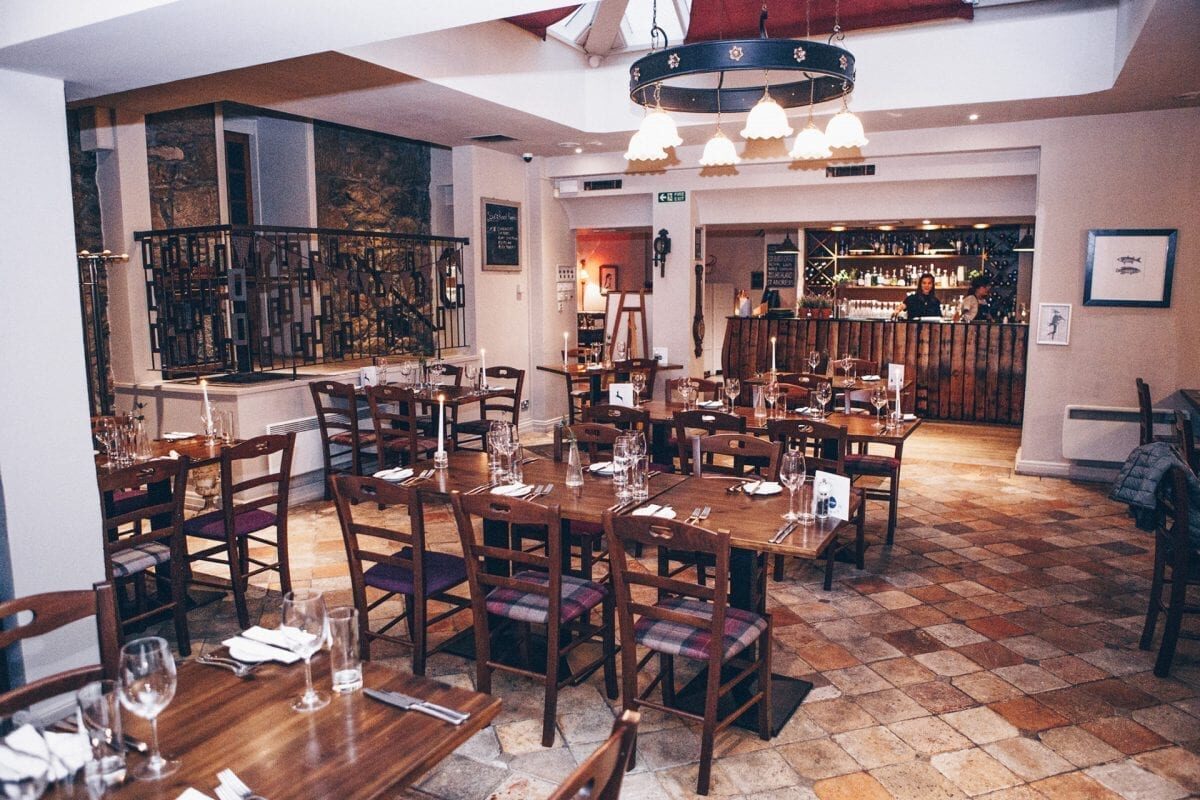 Restaurant dining room with laid tables, wrought-iron balustrade and stocked bar behind