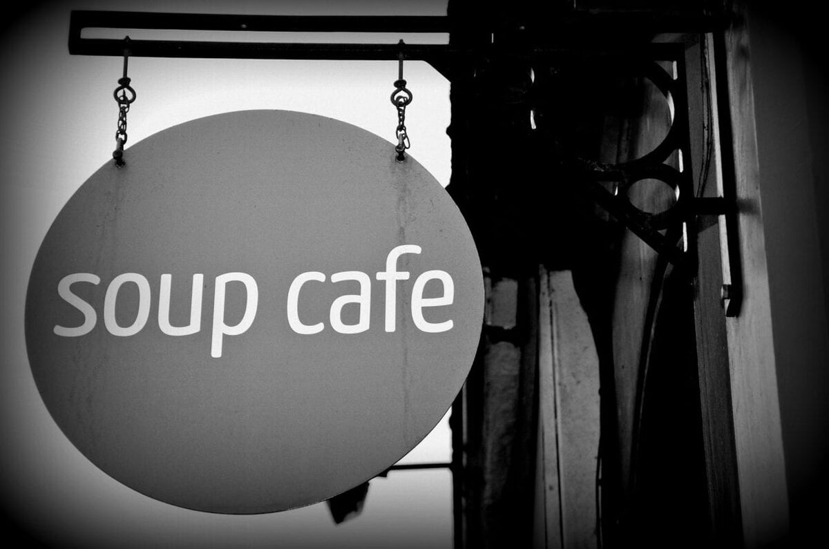 Round hanging sign reading "soup cafe" outside a shopfront in black and white