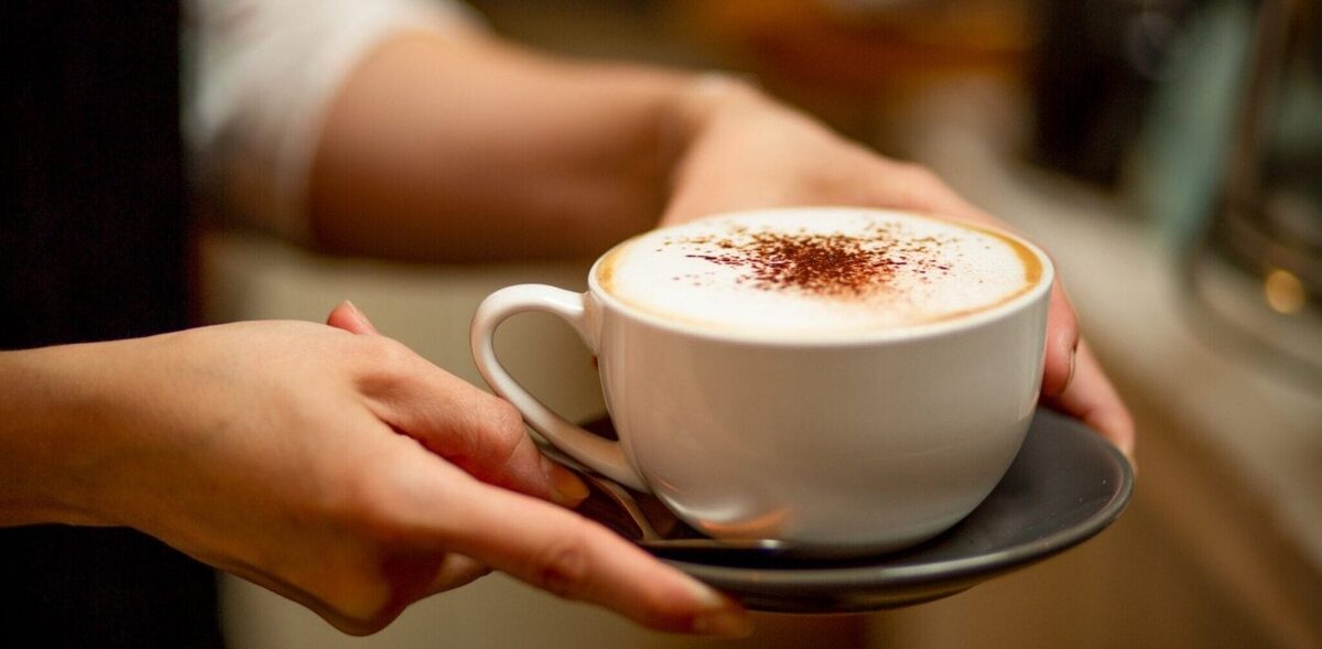 Hands presenting a cappuccino dusted with cocoa in a white cup