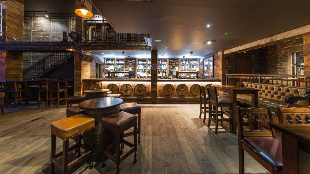 Whisky barrels line the bar counter beneath shelves of bottles and a mezzanine level