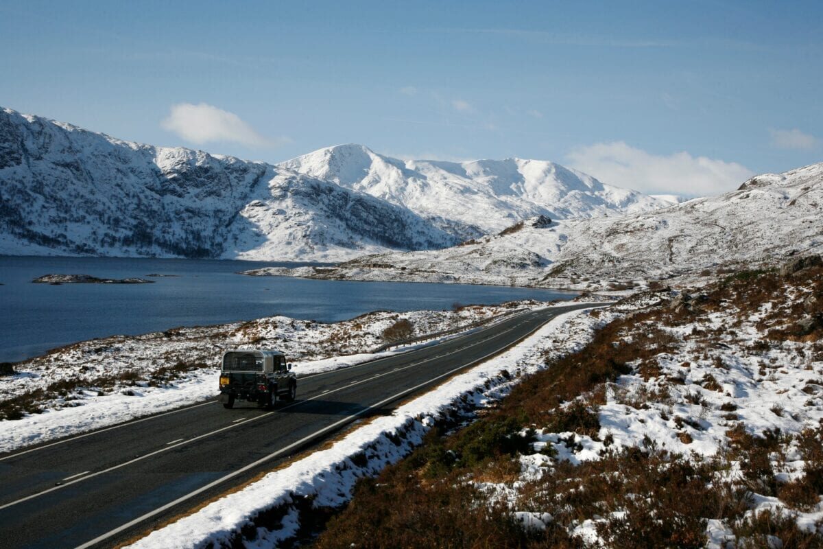 The A87 running beside Loch Cluanie under snow-covered mountains, a car on the road.