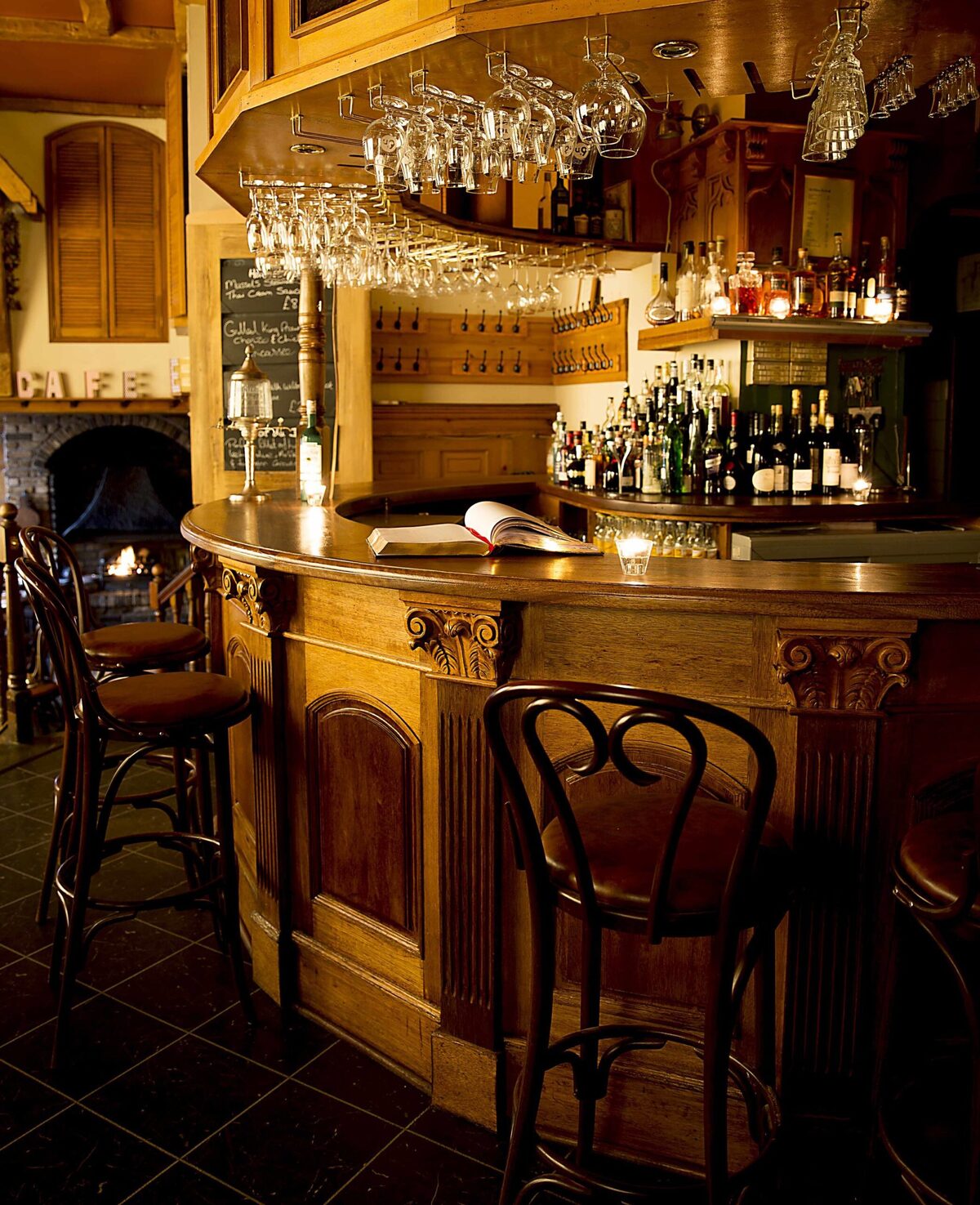 Wooden bar with hanging wine glasses, bottles and a lit fireplace