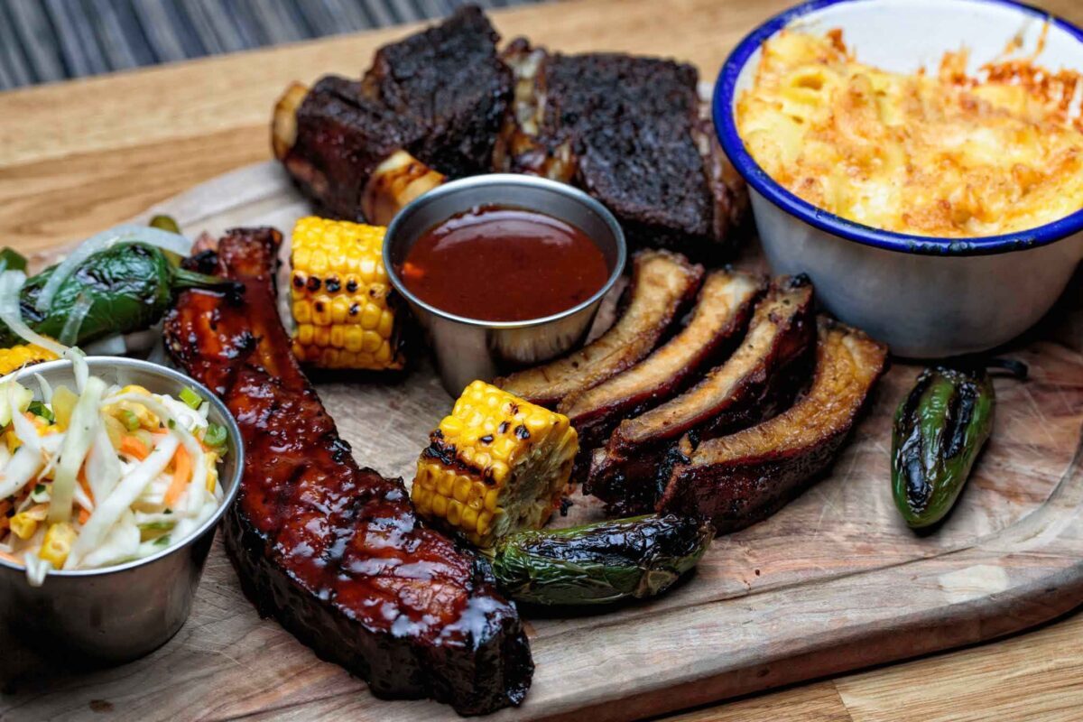 Wooden board with ribs, brisket, corn, coleslaw, sauce and macaroni cheese