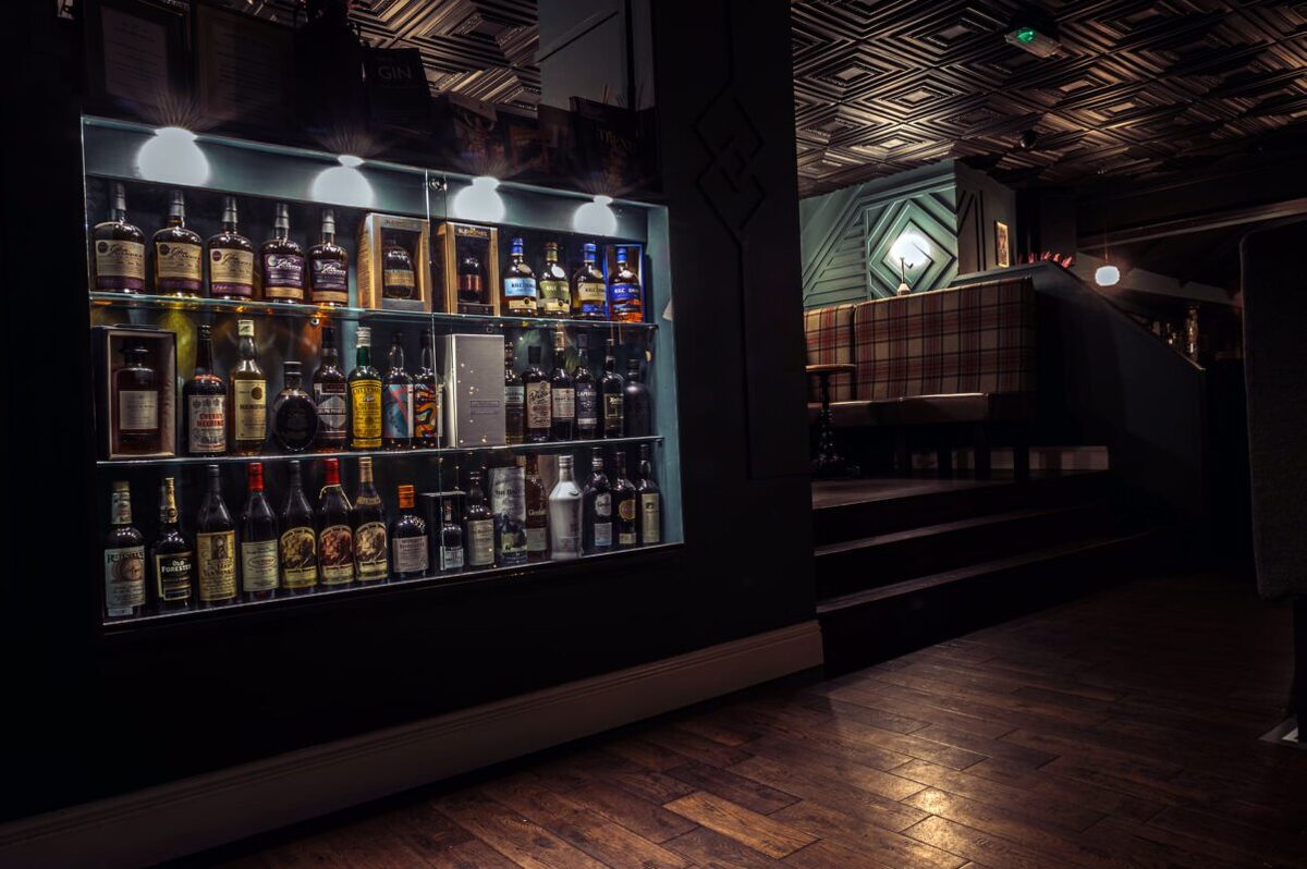 Whisky bottles lit on shelves beside a tartan booth and patterned ceiling