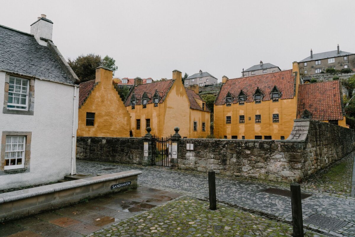 Ochre crow-stepped gabled houses line a cobbled street beside a stone wall