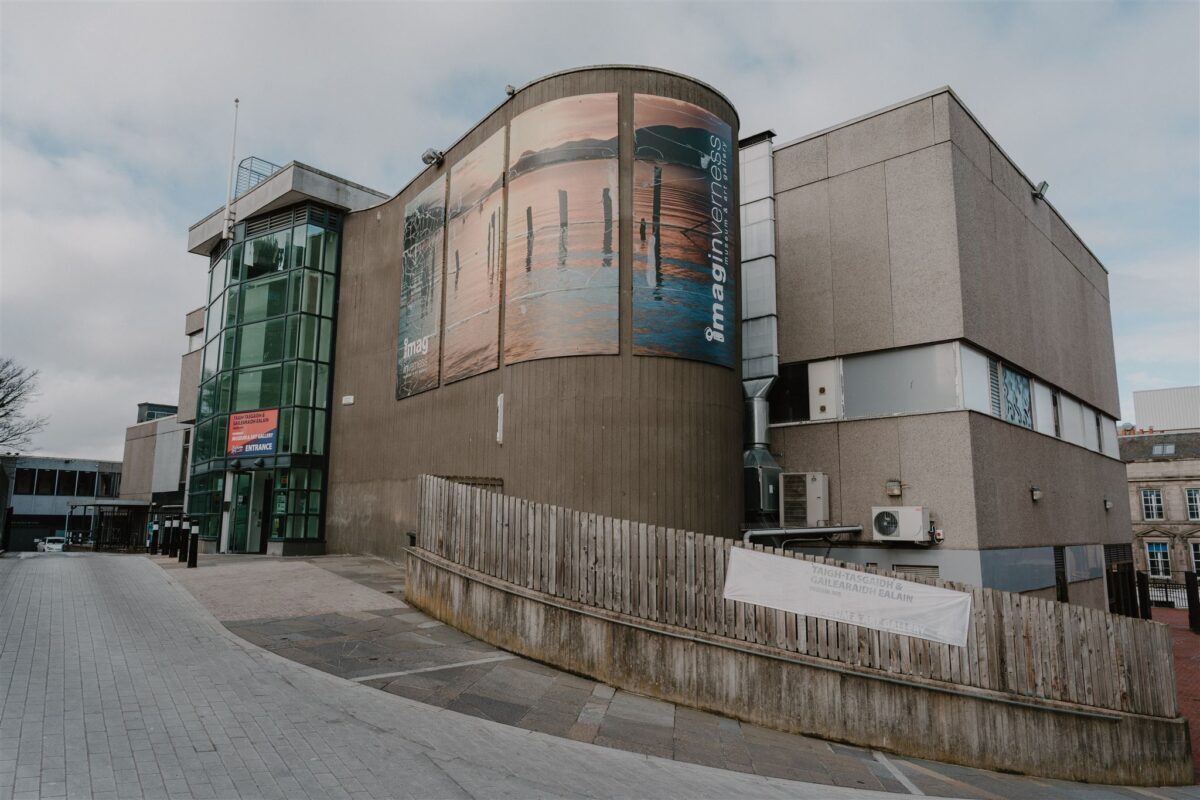 Curved building with large "Imaginarium" banner above a wooden fence
