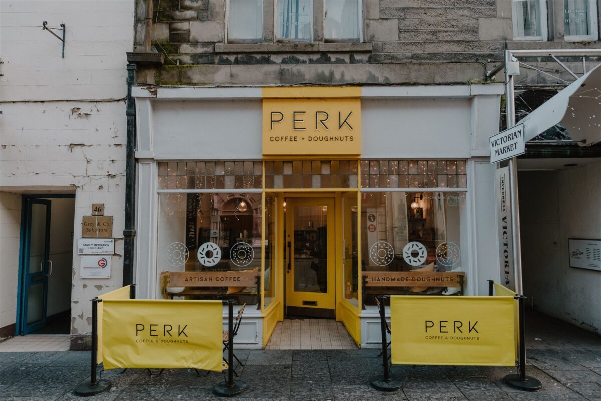 Yellow shopfront of Perk Coffee and Doughnuts, with pavement A-boards outside