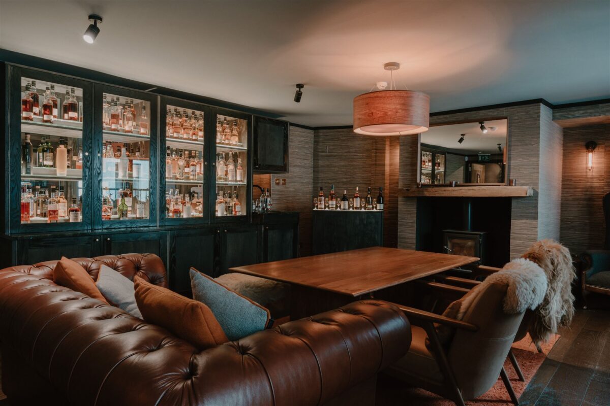 Leather sofas face a fireplace beside glass cabinets stocked with whisky bottles