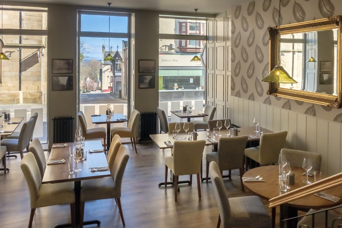 Restaurant tables laid with cutlery beside large windows overlooking the street