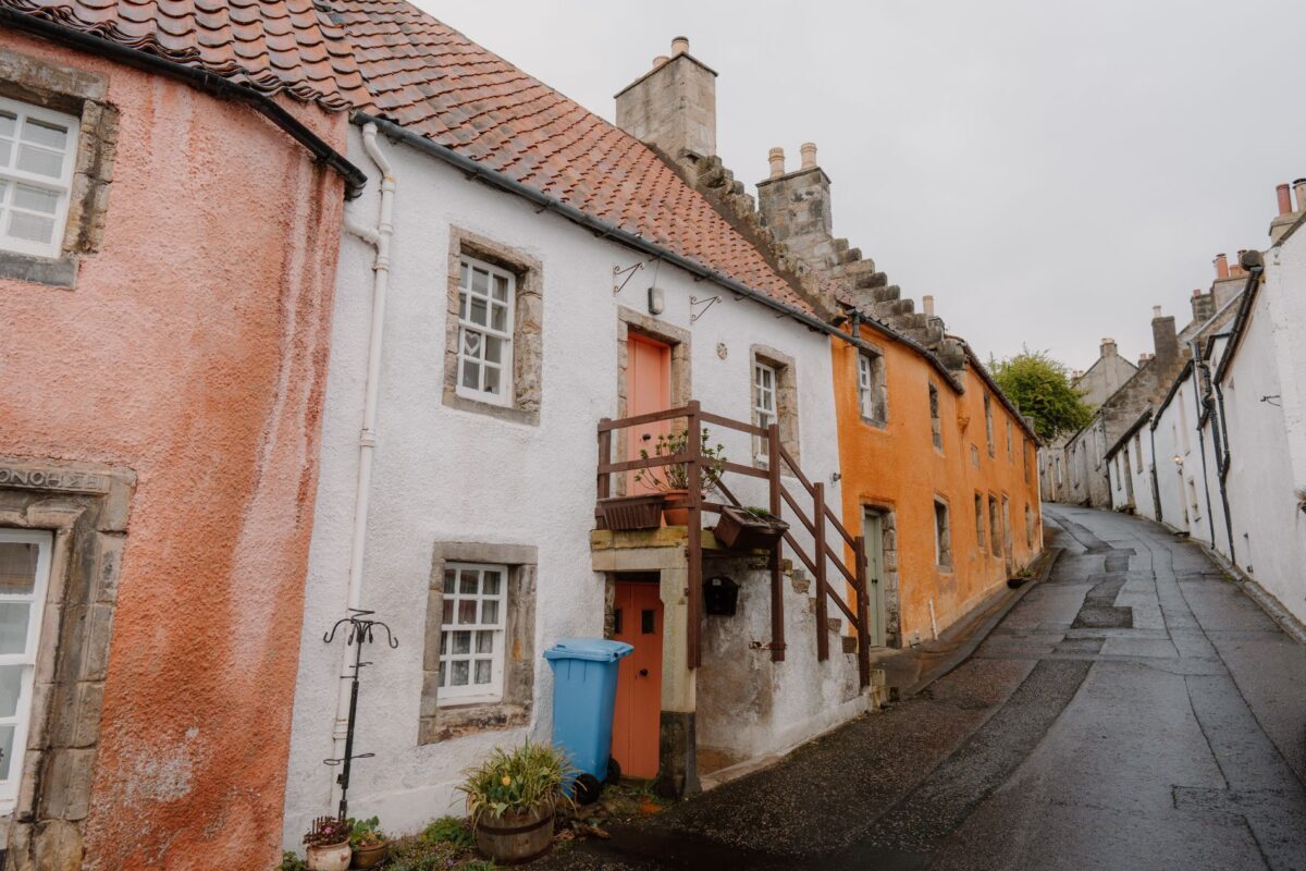 Pink, white and ochre cottages line a narrow cobbled street in the rain