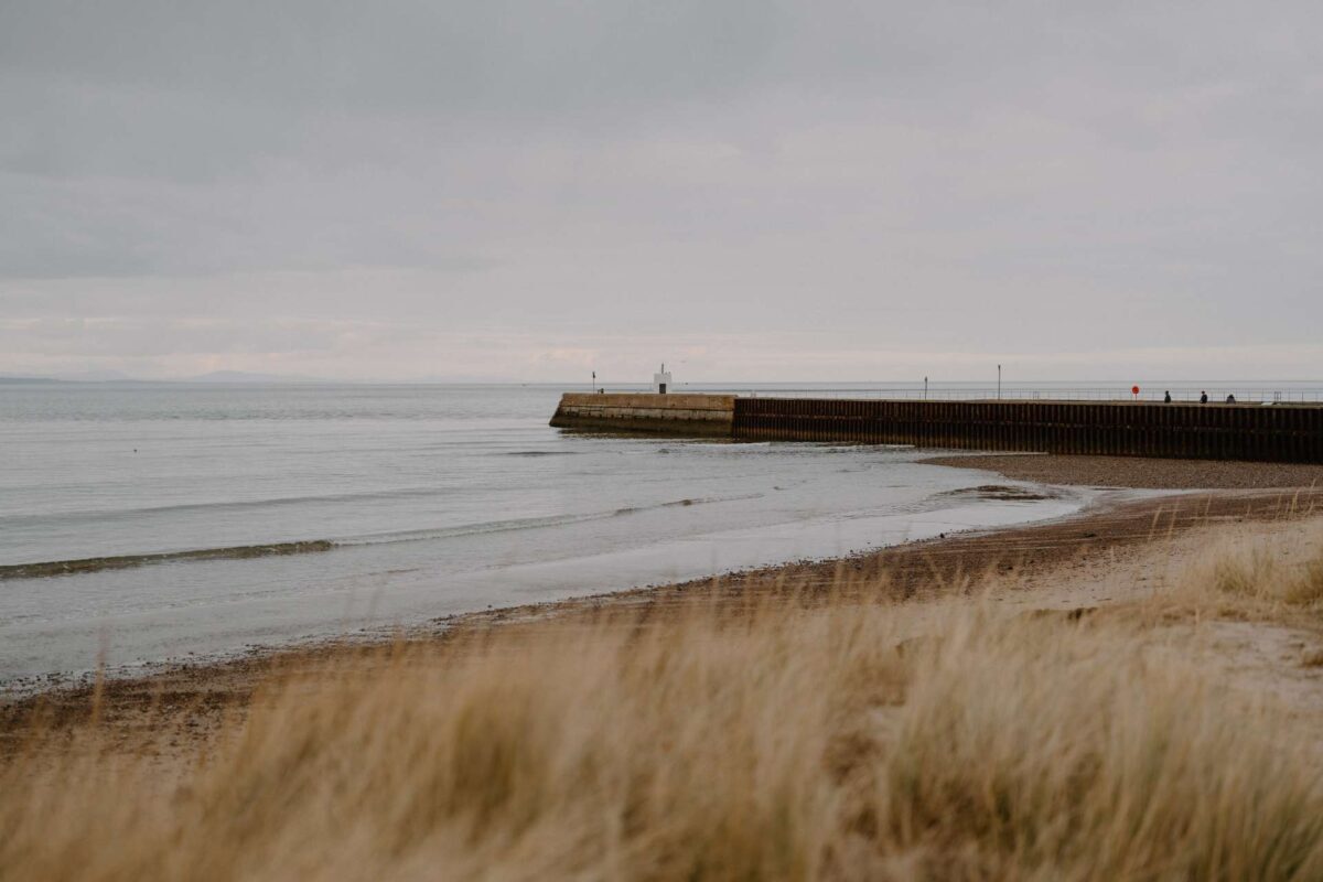 Long stone pier stretches into the sea beyond a grassy dune