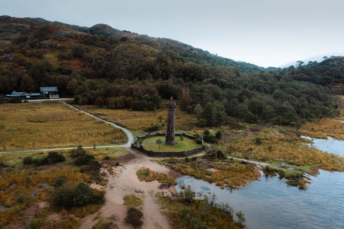 The Glenfinnan Monument from the air, its paths and the head of Loch Shiel among autumn hills.