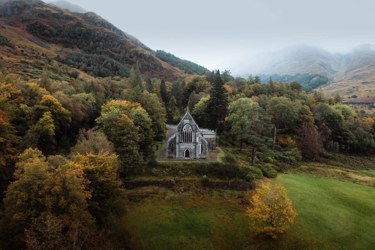 The Gothic church of St Mary and St Finnan among autumn trees on the hillside at Glenfinnan, hills behind.