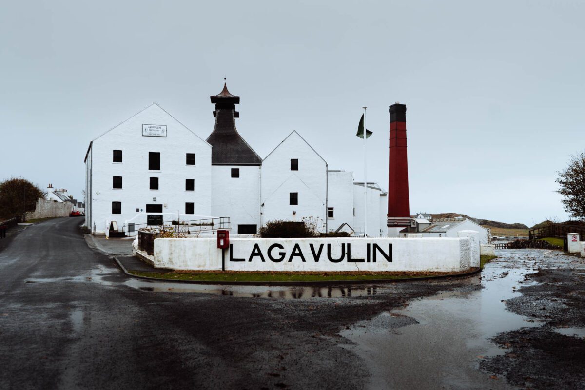 The white front of Lagavulin with its name on the wall and the red chimney behind.