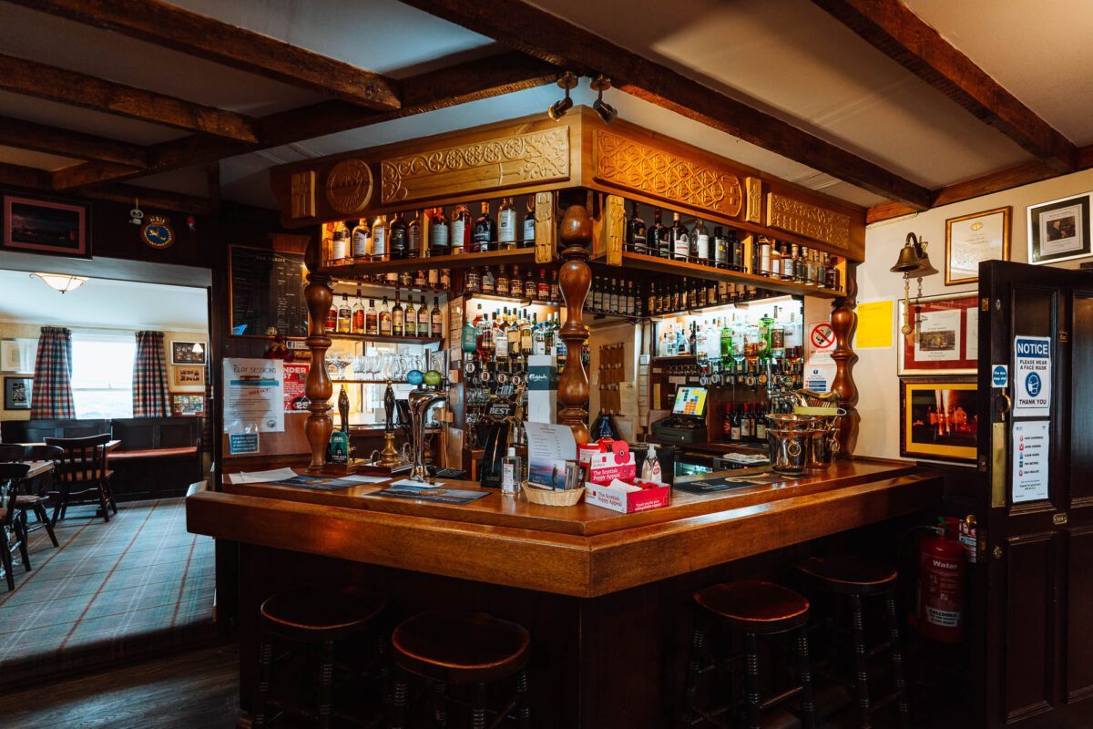 The bar of the Port Charlotte Hotel, whisky bottles lined up behind a carved wooden counter.