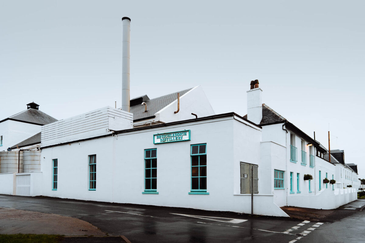 White-washed Bruichladdich Distillery buildings with turquoise-framed windows and a tall chimney