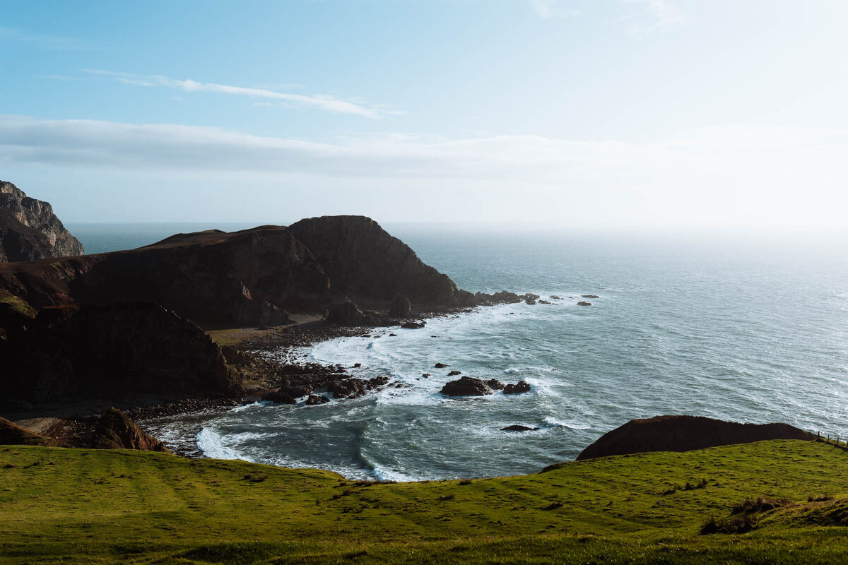 A dark headland and a rocky cove at the Mull of Oa, the sea bright beyond.