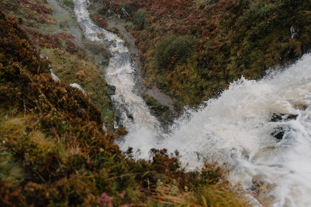 Waterfall cascading through rocky gorge lined with autumn heather and ferns
