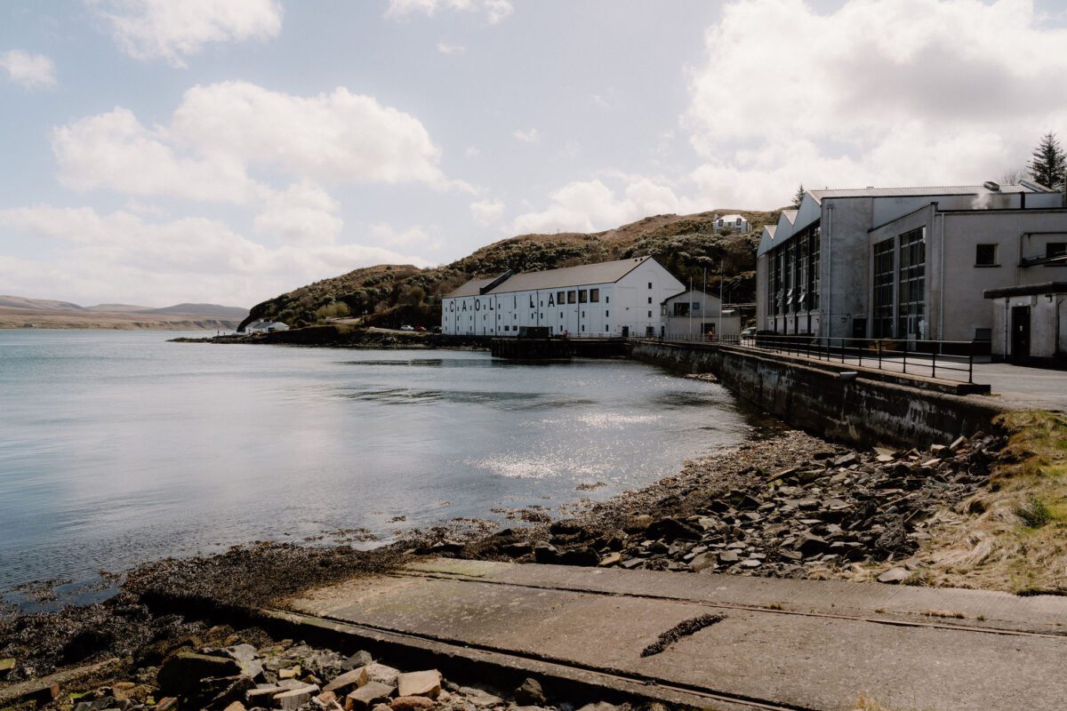 White harbourside buildings beside a rocky shore and calm loch under hills