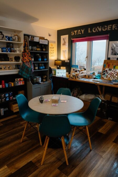 Round table and teal chairs beneath "Stay Longer" lettering in a gift shop café