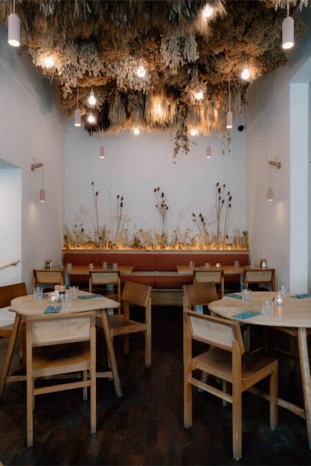 Restaurant interior with dried flowers covering the ceiling and pendant lights above wooden tables