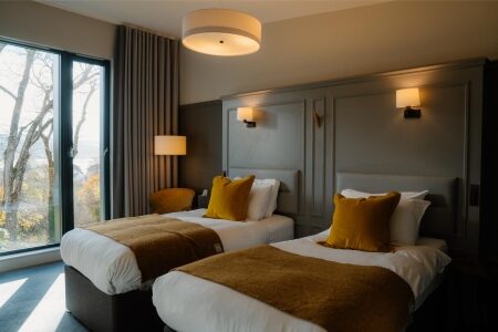 Twin beds with mustard cushions and throws beside a large window