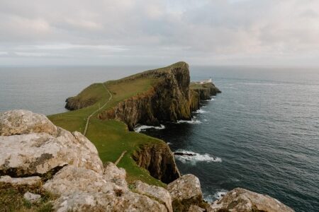 Grassy headland leads to a distant lighthouse at Neist Point, Skye