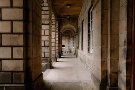 Stone colonnade with arched ceiling and windows along a covered walkway