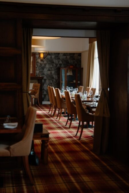 Dining room with tartan carpet, wine glasses set on long wooden tables