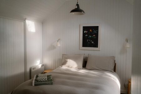 Attic bedroom with white panelled walls, double bed and framed floral print