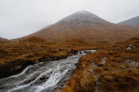 Small waterfall tumbling through moorland beneath a snow-dusted conical peak
