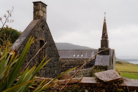 Stone chimney gable and church spire behind a moss-covered wall