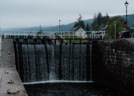 Water cascades through canal lock gates towards a white cottage beyond