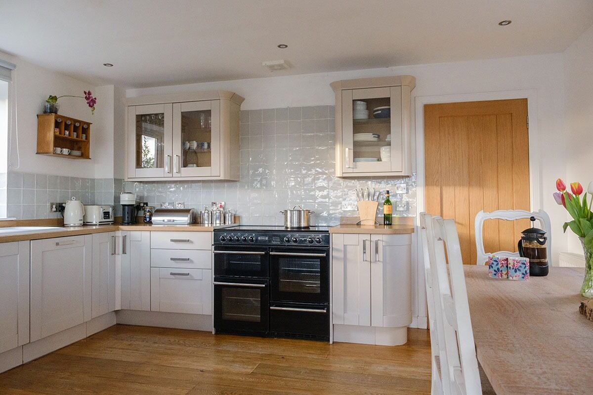 A kitchen with cream cabinetry and a black range cooker, tulips on the table to the right and glass-fronted cupboards above the counter.