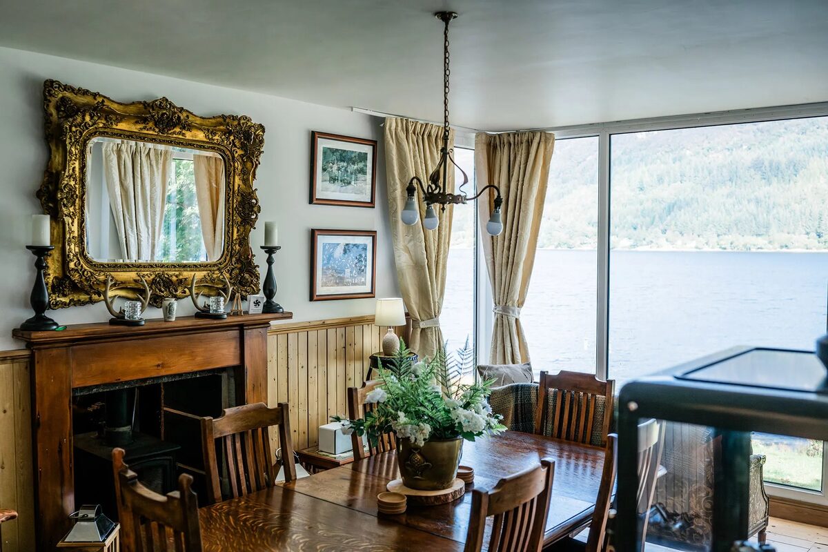 An antler chandelier hangs above leather armchairs with red cushions, a wood burning stove and gilt mirror completing the sitting room.