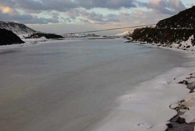 Frozen loch surrounded by snow-dusted hills under a cloudy sky
