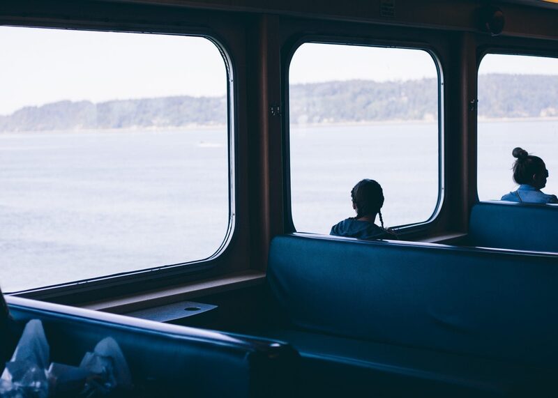 Passengers seated by ferry windows overlooking calm water and distant hills