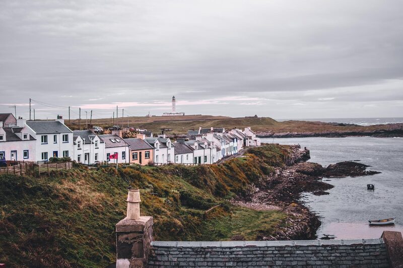 White cottages line a clifftop row with a lighthouse in the distance