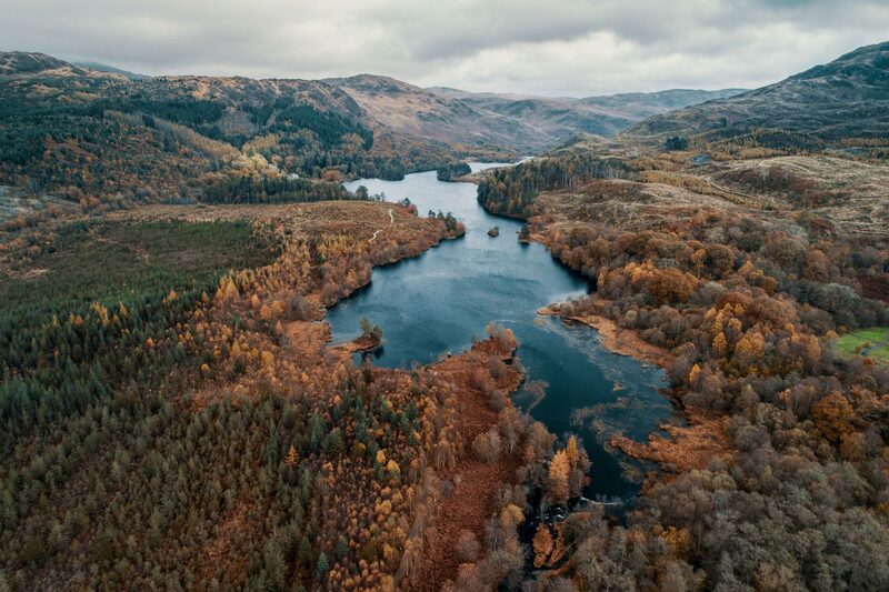 Aerial view of a winding loch surrounded by autumn woodland and hills