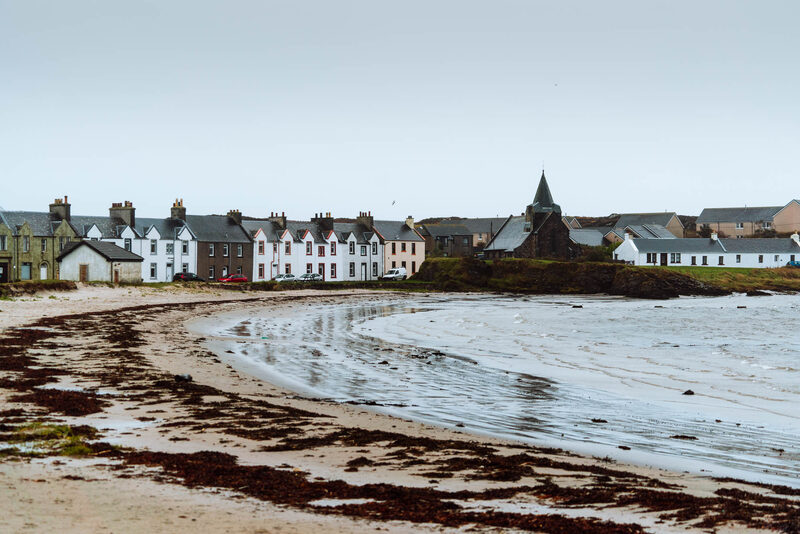 Whitewashed terraced houses and a church spire overlook a seaweed-strewn beach